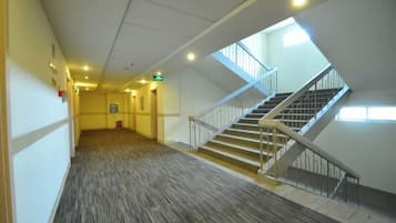 A corridor with a carpeted floor, a staircase with a handrail, and a door with an emergency exit sign.
