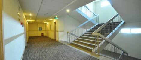 A corridor with a carpeted floor, a staircase with a handrail, and a door with an emergency exit sign.