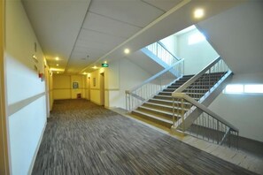 A corridor with a carpeted floor, a staircase with a handrail, and a door with an emergency exit sign. - Jinjiang Inn (LinyiWanxianghui Railway Station Hotel) (Linyi)