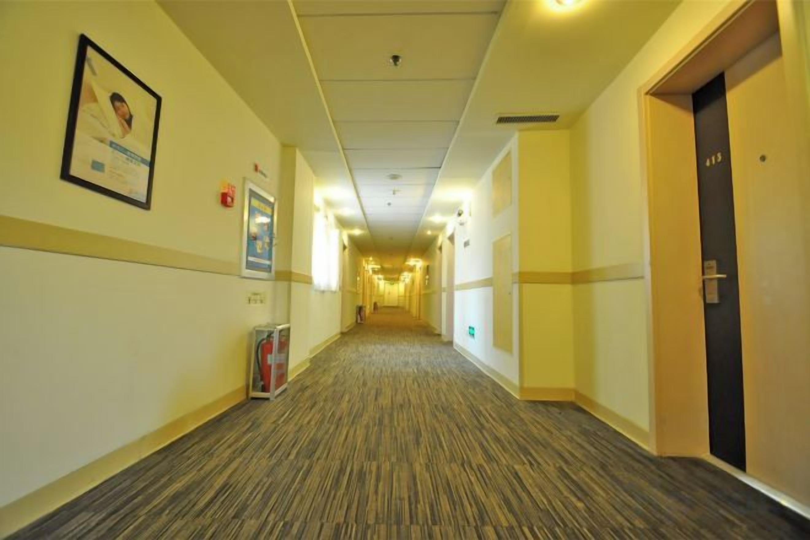 A hotel corridor with a carpeted floor, framed pictures on the walls, and doors on the right.