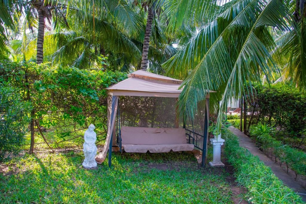 Un área de estar al aire libre cubierta con un banco y una estatua, rodeada de exuberante vegetación y palmeras.