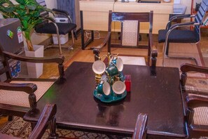 Ein Essbereich mit einem dunklen Holztisch, umgeben von vier Stühlen mit gepolsterten Sitzen. Auf dem Tisch steht ein dekorativer Metallständer mit Tellern und einer Tasse.