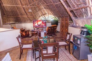 A room with a thatched roof, wooden furniture, a television, and a refrigerator. - Jumbo Art Sign Villa (Diani Beach)