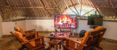 Quarto aconchegante com telhado de palha, televisão, móveis de madeira e uma pequena mesa.