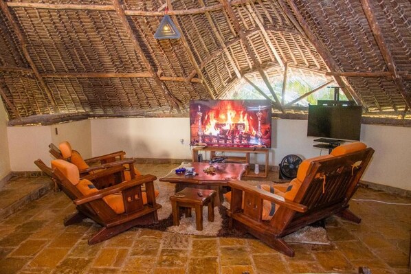 Una habitación acogedora con techo de paja, televisor, muebles de madera y una pequeña mesa.