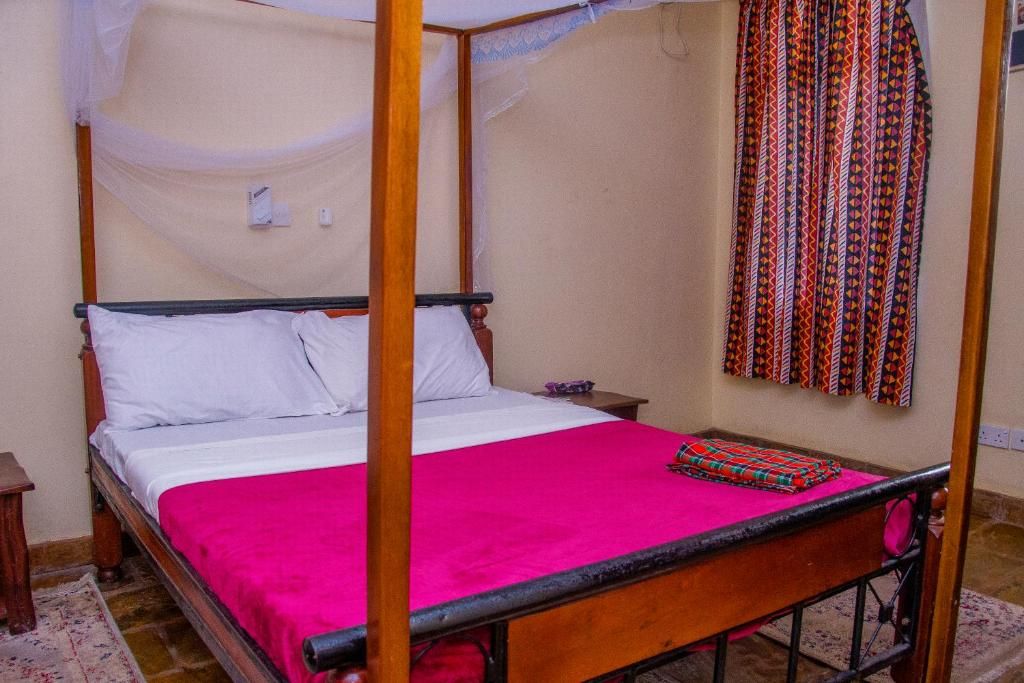 Una cama con dosel, ropa de cama blanca, y una colcha rosa.