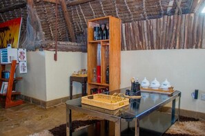 A rustic interior with a wooden bookshelf, a glass-top table, and a woven basket. - Jumbo Art Sign Villa (Diani Beach)