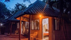 En mysig bungalow med ett tak täckt av tegelpannor, en veranda med stolar och en säng som syns genom en öppen dörr.