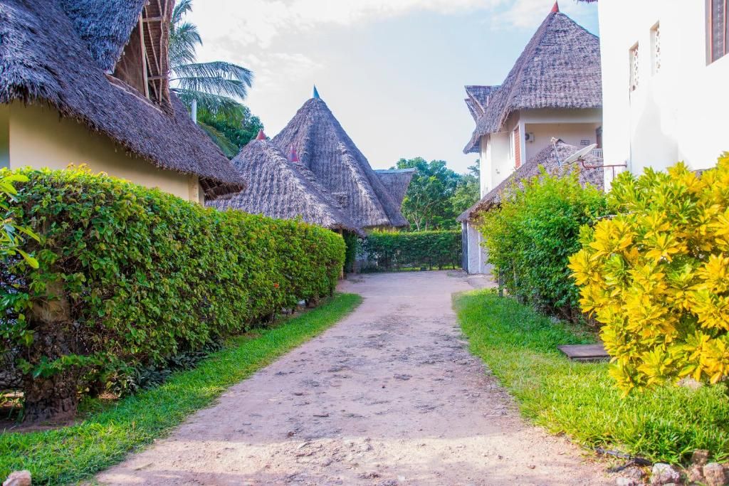 Un sentier qui mène à des maisons traditionnelles à toits de chaume, entourées d’une végétation luxuriante.