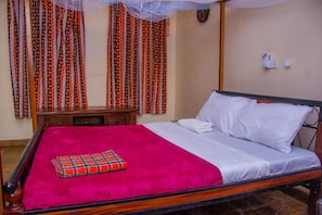 A single bed with a red blanket and a plaid pillow, a wooden nightstand, and curtains with a geometric pattern. - Jumbo Art Sign Villa (Diani Beach)