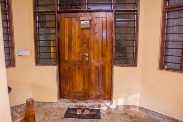 A wooden door with a sign that reads 'Home Sweet Home' and a pair of shoes on a mat in front. - Jumbo Art Sign Villa (Diani Beach)