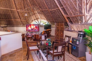 A room with a thatched roof, wooden furniture, a television, and a refrigerator. - Jumbo Art Sign Villa (Diani Beach)