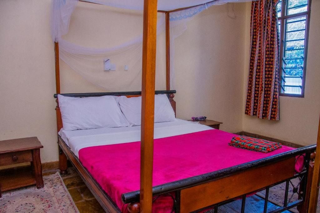 Ein Himmelbett mit Baldachin, ein Nachttisch und ein Fenster mit gemusterten Vorhängen.