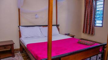 Ein Himmelbett mit Baldachin, ein Nachttisch und ein Fenster mit gemusterten Vorhängen.