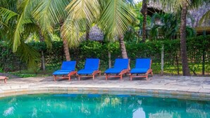 Zona de piscina con sillas reclinables azules y palmeras.