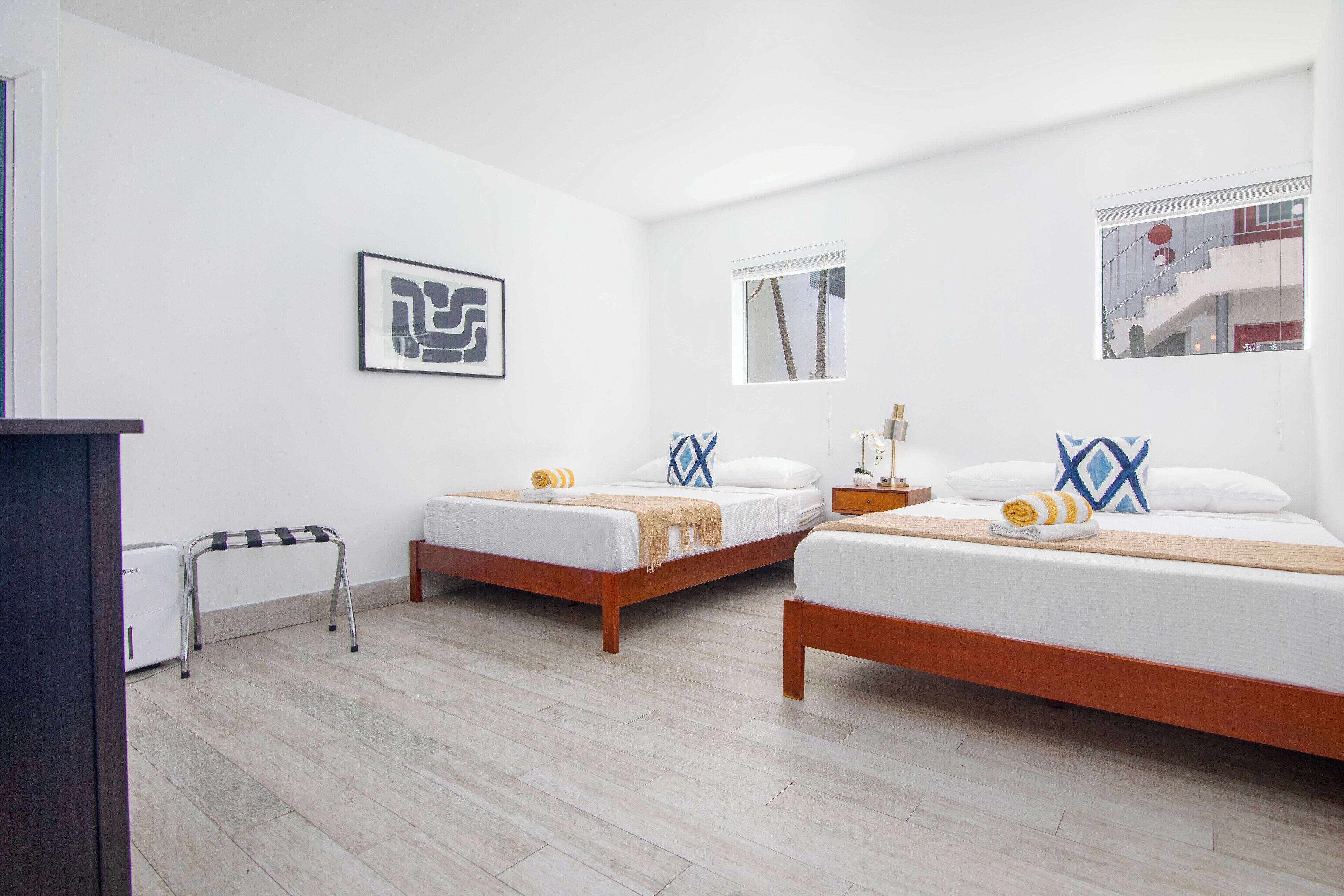 Una habitación de hotel con dos camas, una mesita, una silla y una ventana.