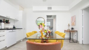 A modern kitchen with white cabinets, a glass dining table, and yellow chairs. - Boutique Apartments SoBe (Miami Beach)