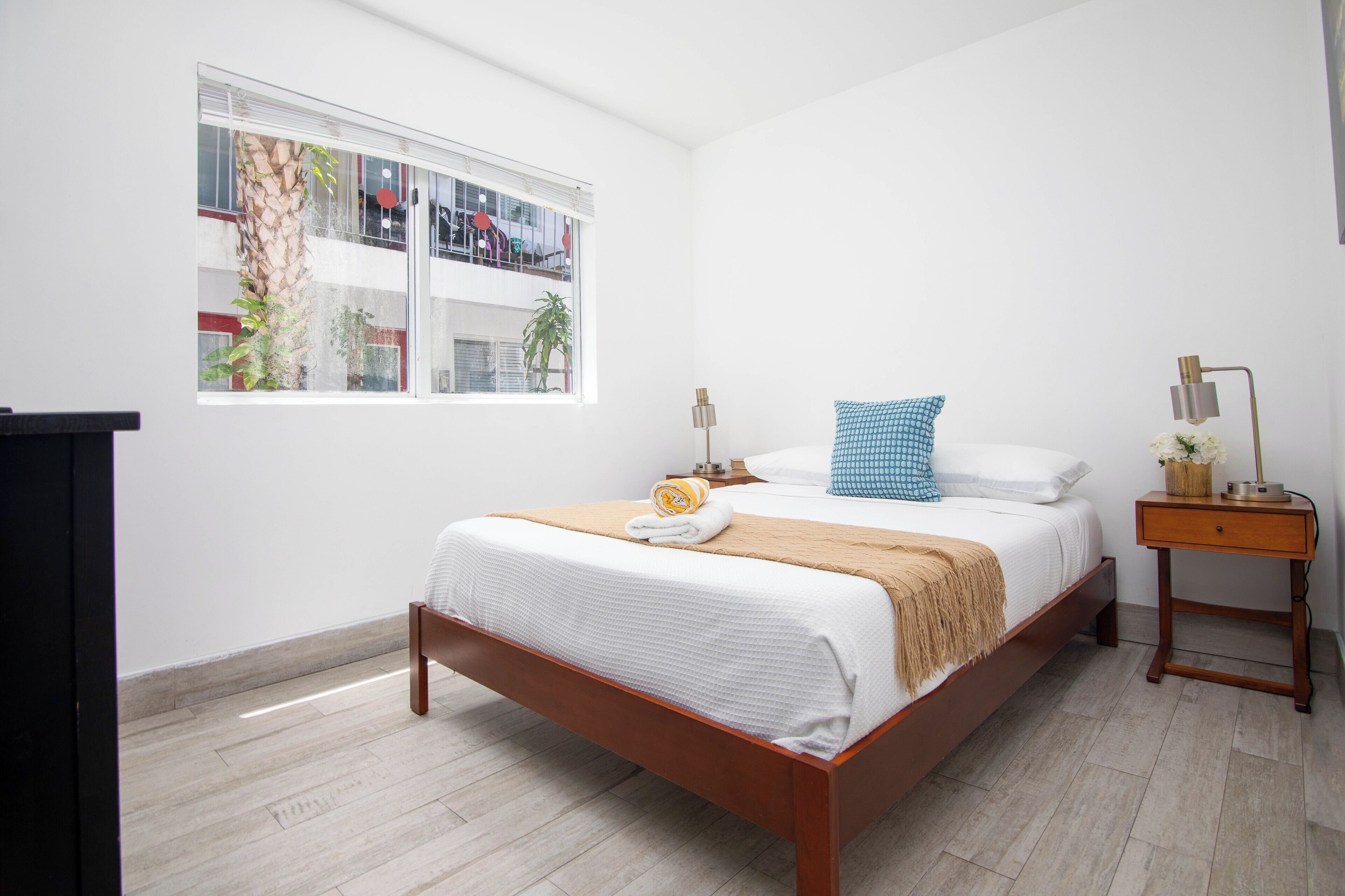 A neatly arranged bedroom with a bed, bedside table, lamp, and window.