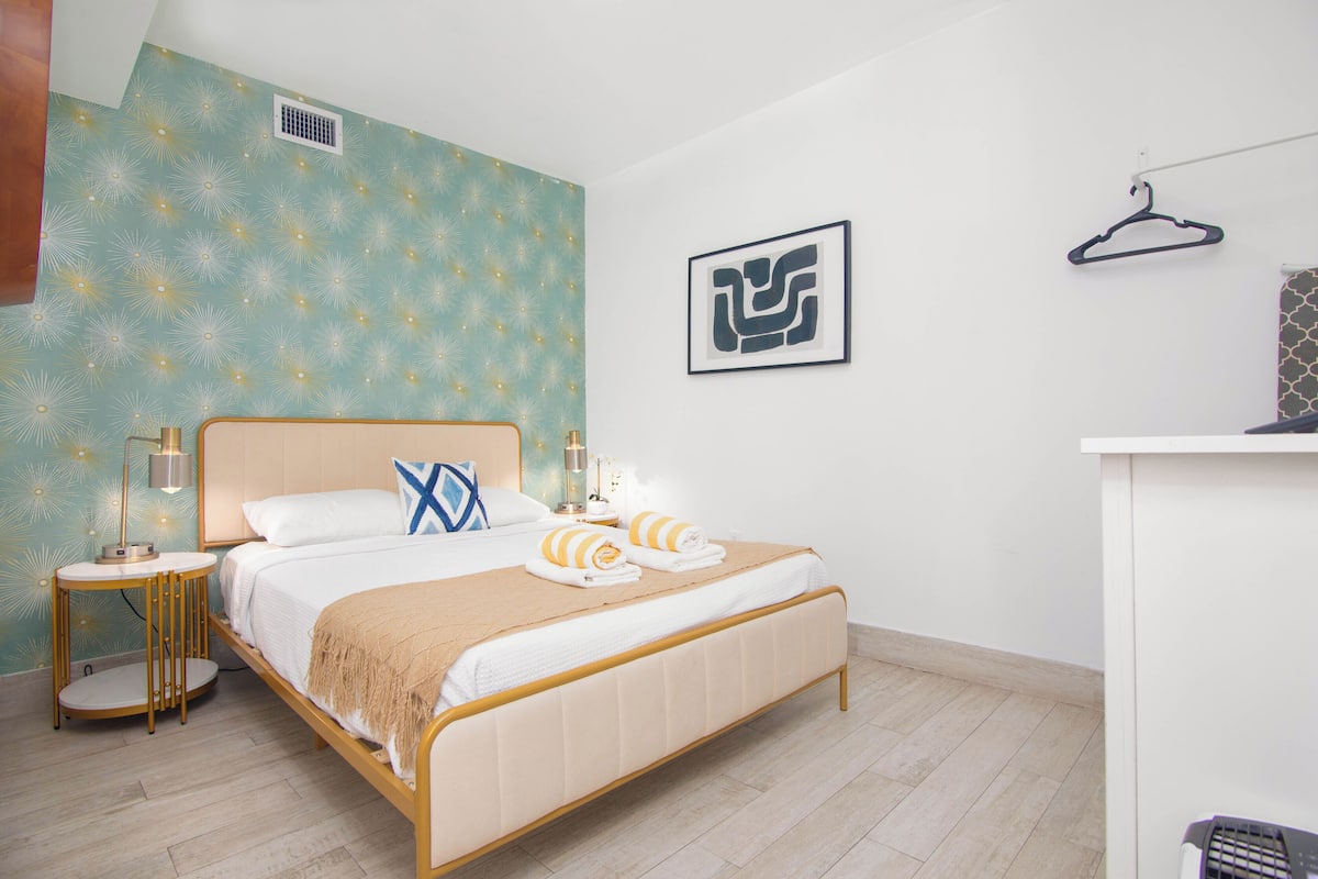Ein modernes Hotelzimmer mit Bett, Nachttischen, einem Kleiderhaken und einer Wand mit geometrischem Muster.