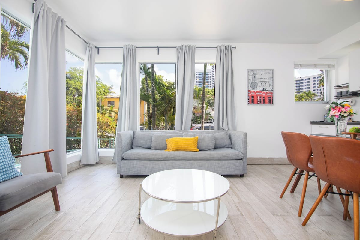 Ein modernes Wohnzimmer mit einem grauen Sofa, einem runden Couchtisch und einem Essbereich mit Stühlen.