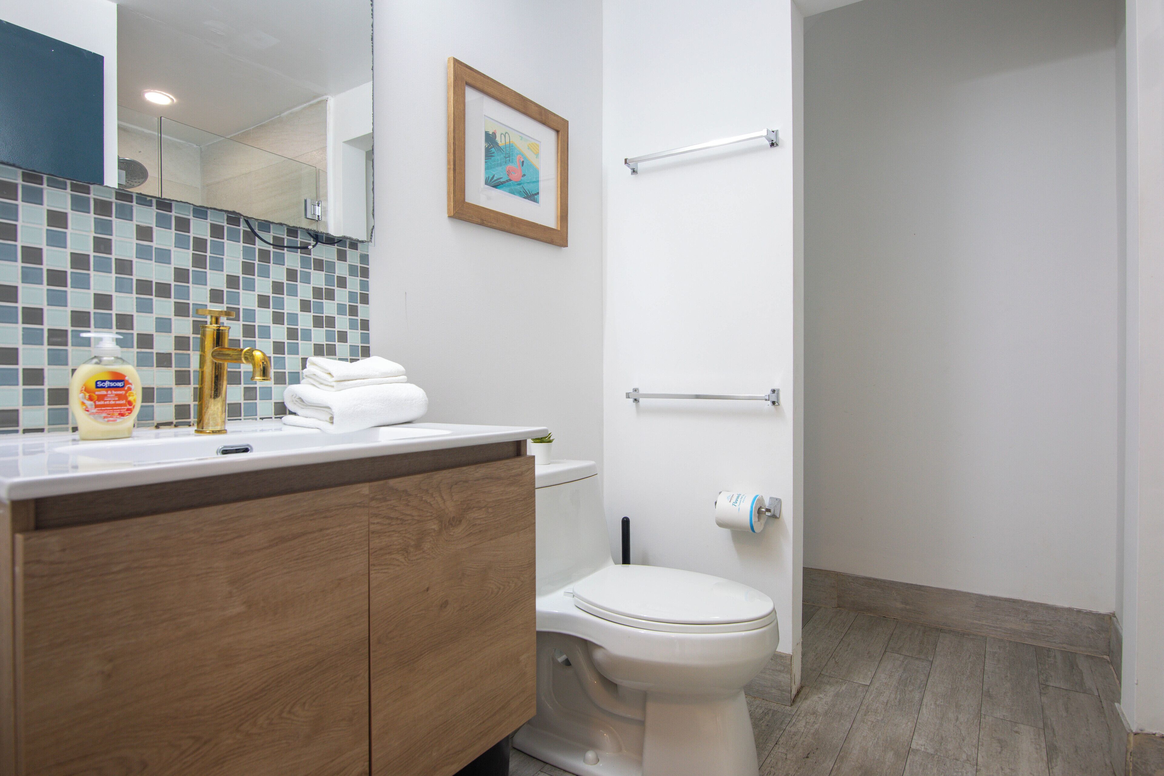 Une salle de bain avec un meuble-lavabo en bois, des toilettes blanches, un tableau encadré au mur et un porte-serviettes.