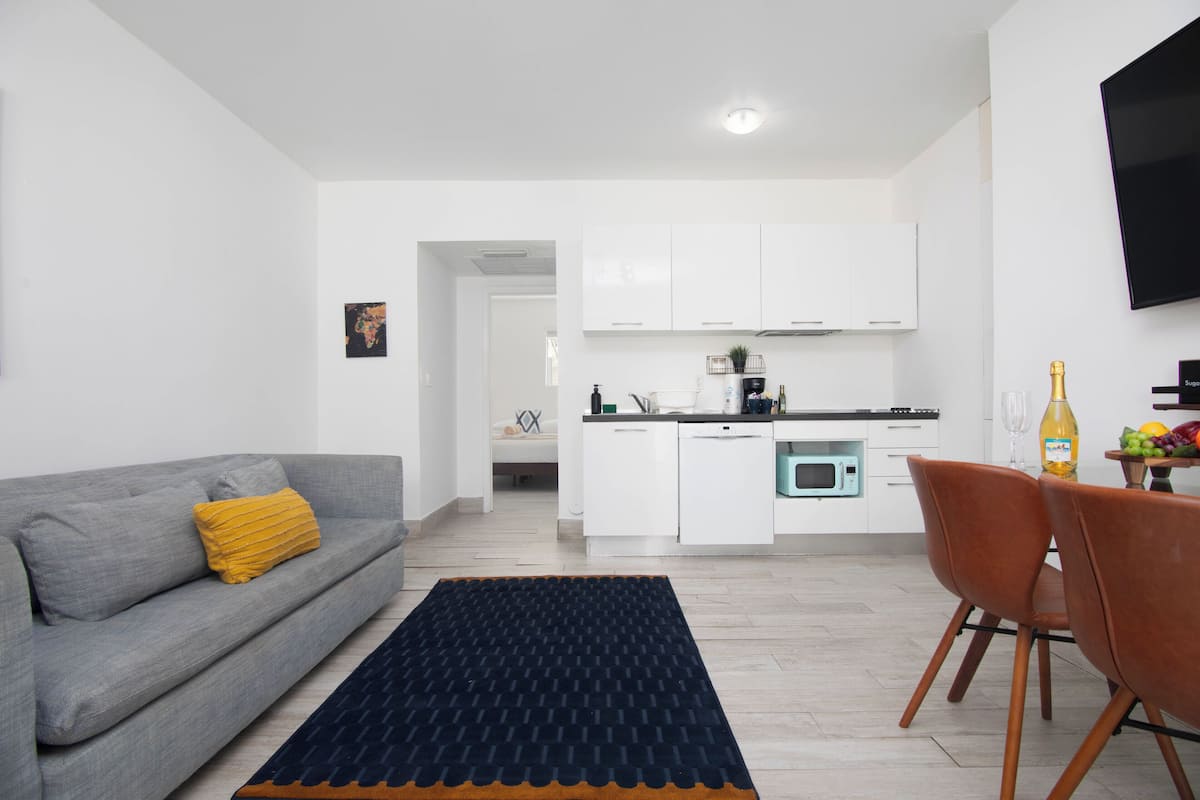 Ein modernes Wohnzimmer mit einem grauen Sofa, einem schwarz-orangenen Teppich und einem Essbereich mit Holzsesseln.