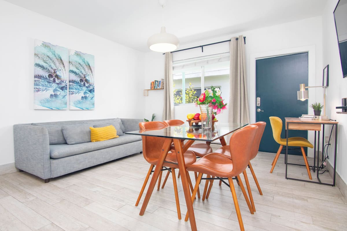 Ein modernes Wohnzimmer mit grauem Sofa, orangefarbenen Sesseln, einem Glastisch und Kunstwerken an der Wand.