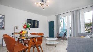 A modern living room with a glass dining table, orange chairs, a grey sofa, and a ceiling light fixture. - Boutique Apartments SoBe (Miami Beach)