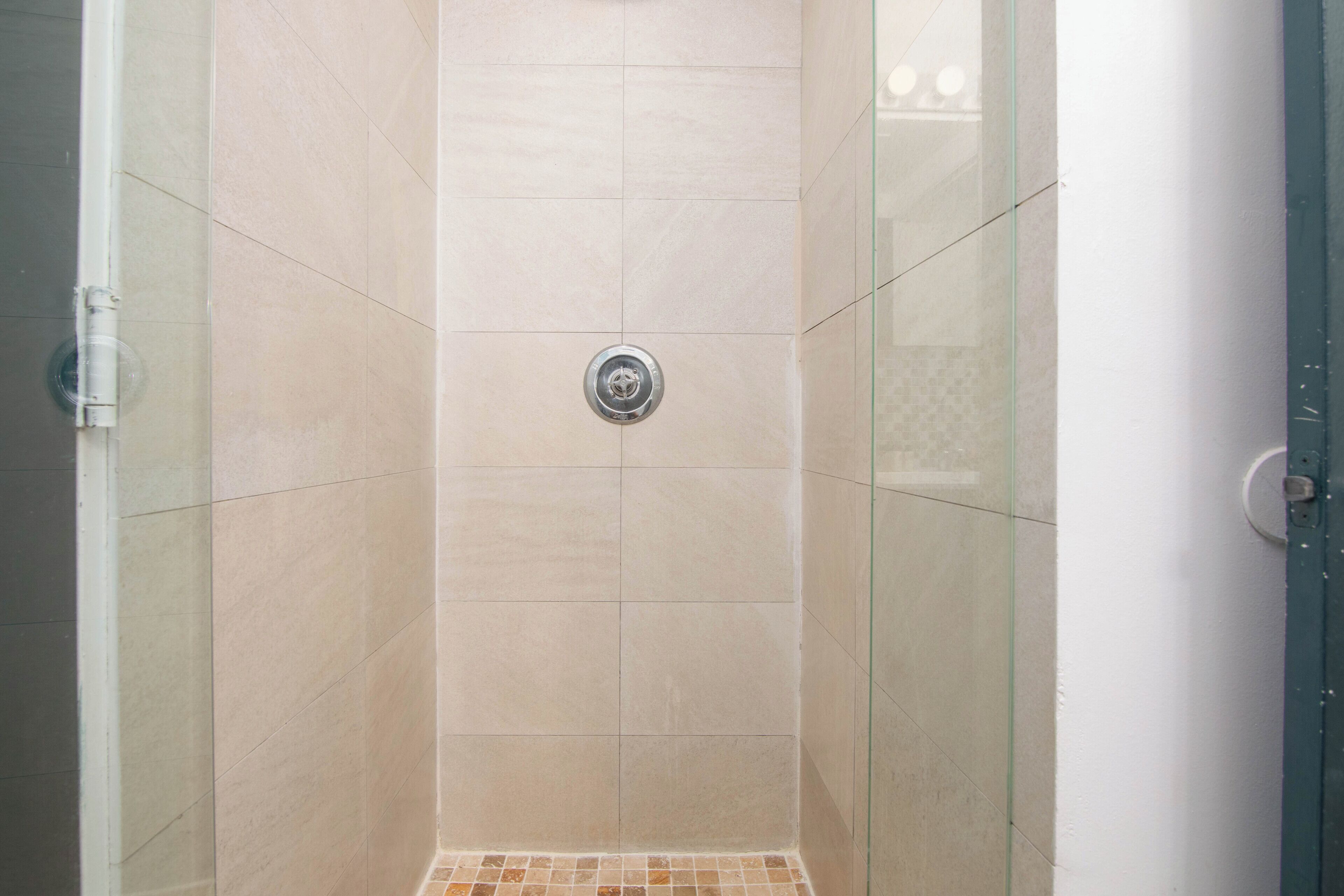 A shower with beige tiles and a glass door.
