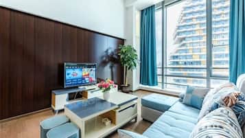 A modern living room with a flat-screen TV, a sofa, a coffee table, and a large window with a city view.
