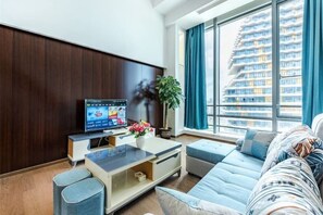 A modern living room with a flat-screen TV, a sofa, a coffee table, and a large window with a city view. - Zhuhai Hengqin Yuyue Apartment (Zhuhai)