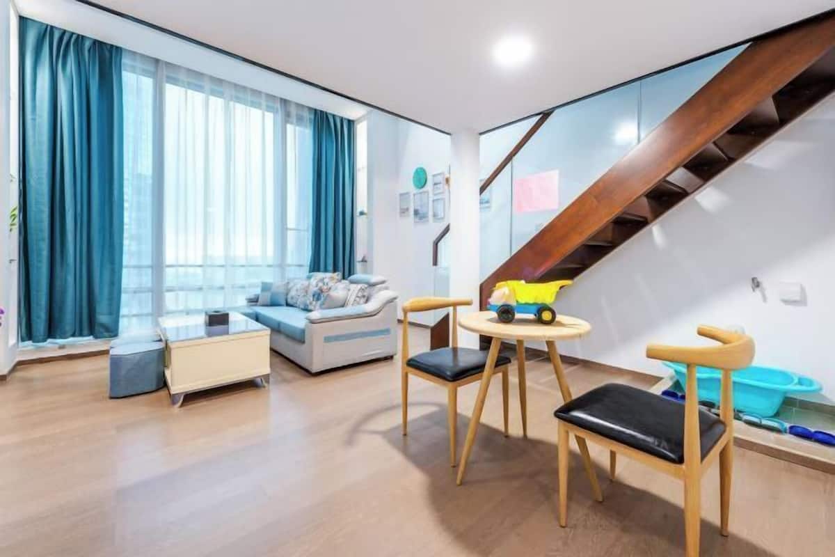 A modern living room with a sofa, a coffee table, two chairs, a staircase, and a window with curtains.