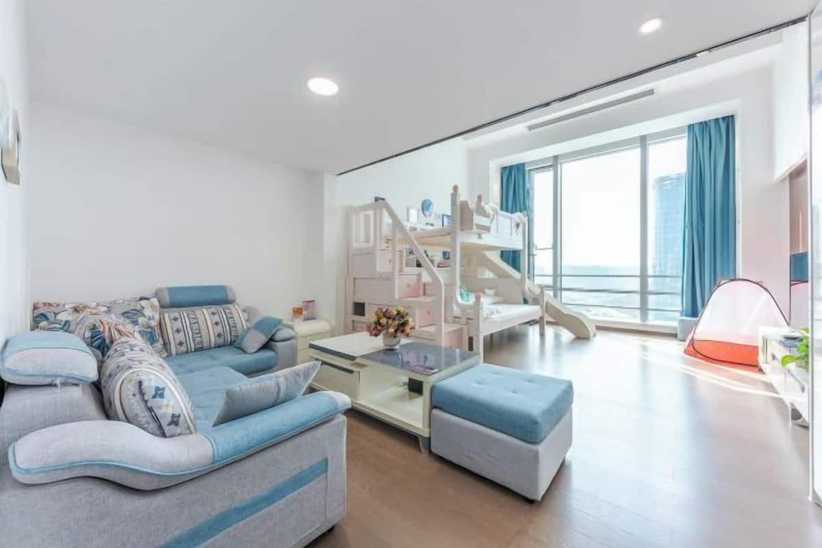 A modern living room with a sofa, ottoman, and a bunk bed with a ladder.