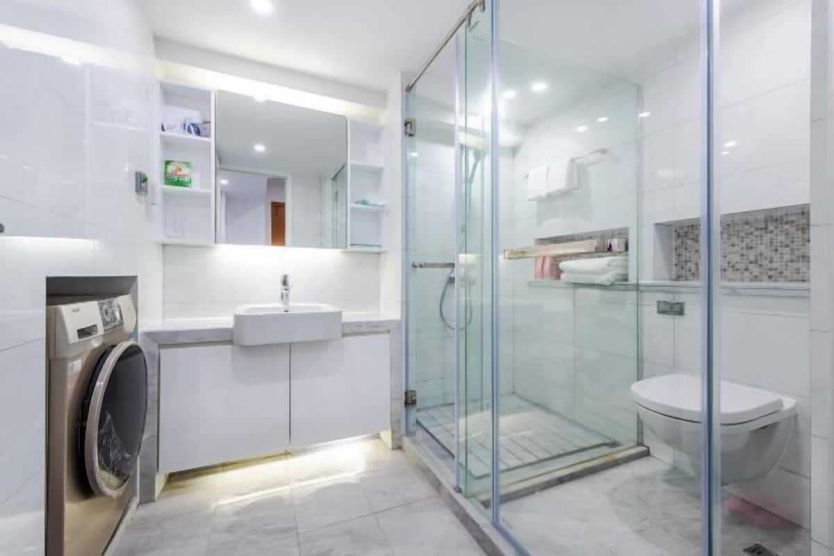 A modern bathroom with a glass-enclosed shower, a built-in sink, and a washing machine.