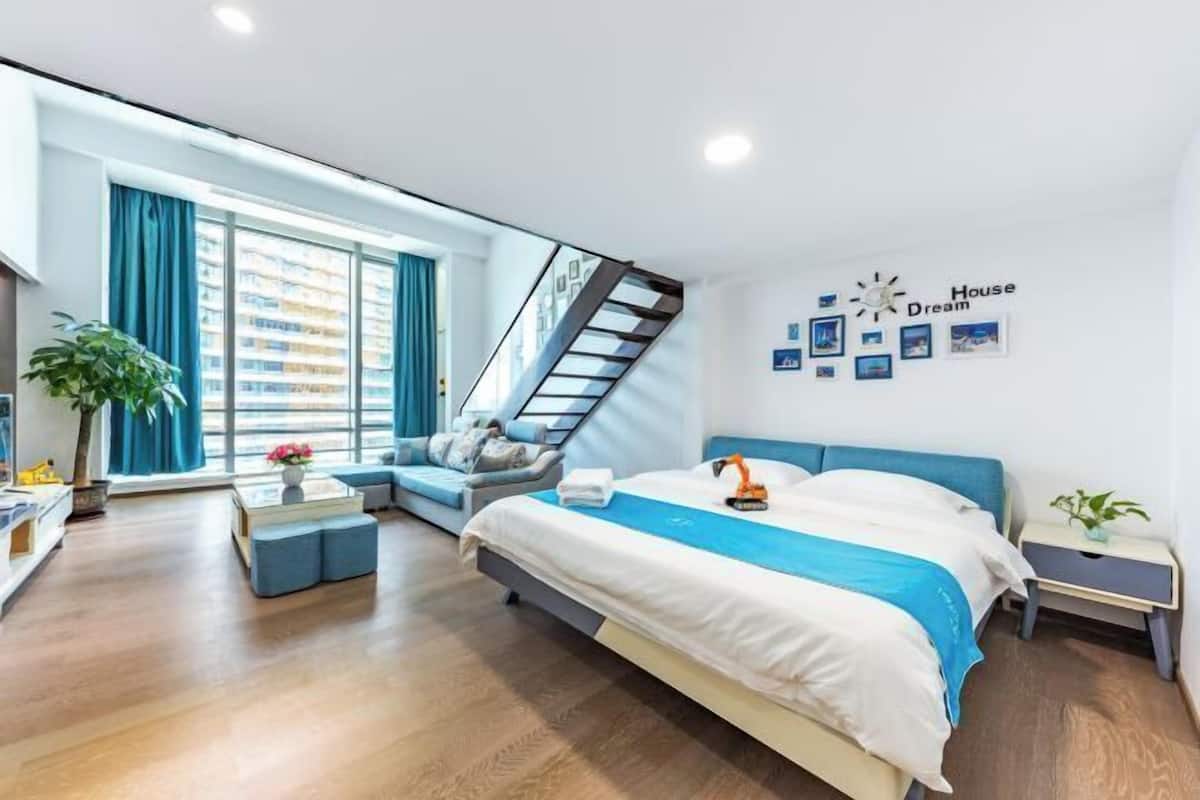A modern bedroom with a bed, a staircase, a sofa, and a wall with pictures and a clock.