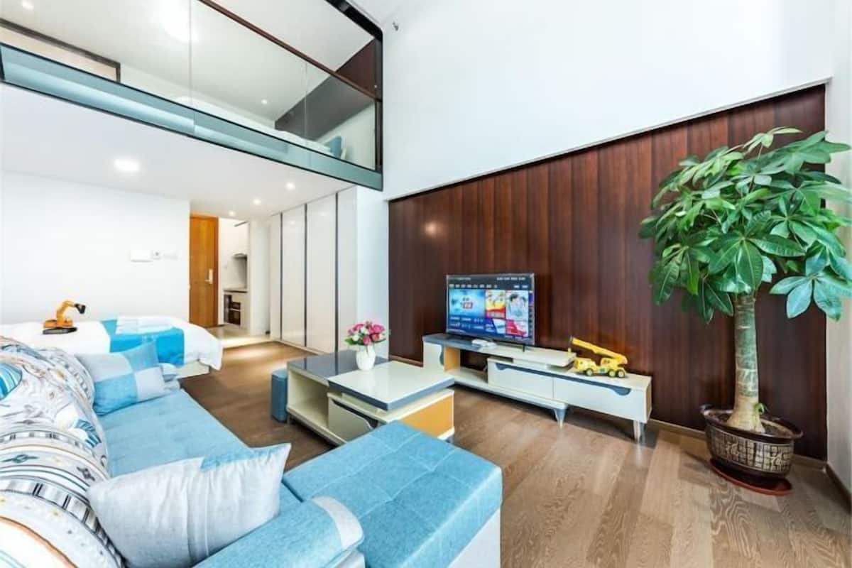 A modern living room with a sofa, television, and a potted plant.