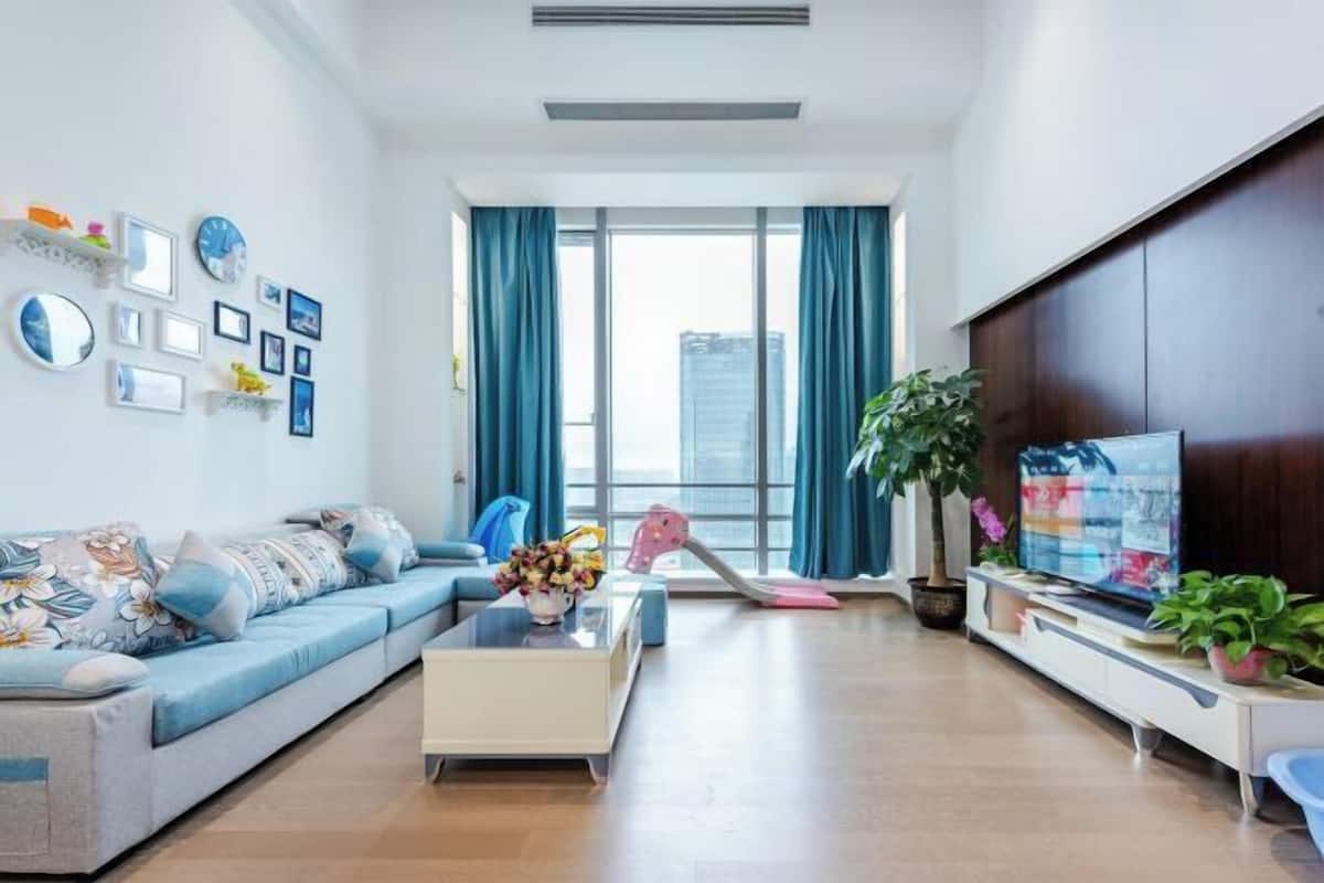 A modern living room with a sofa, coffee table, TV, and large windows with curtains.