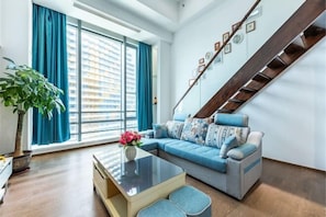 A living room with a sofa, a coffee table, a plant, and a staircase. - Zhuhai Hengqin Yuyue Apartment (Zhuhai)