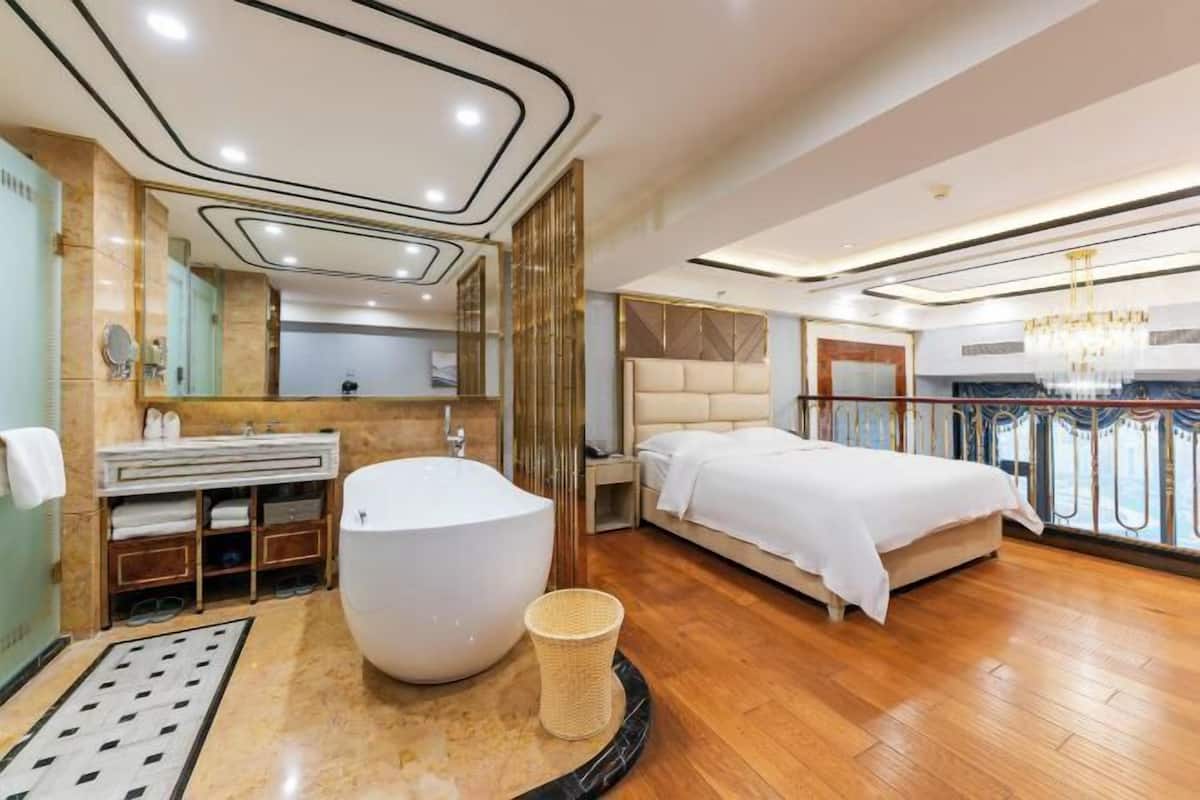 A modern hotel room with a large bathtub, a bed, a vanity with a mirror, and a balcony with a railing.