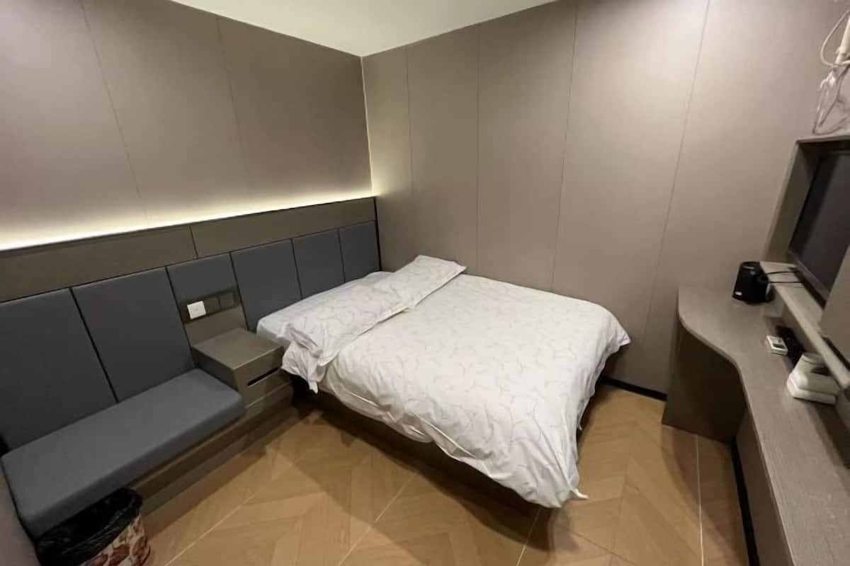 A compact hotel room with a bed, a bench, and a desk with a computer.
