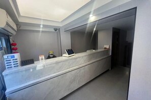 A reception desk with a digital screen, a telephone, and a small table with a cup and a book. - Chuanying Fashion Hotel (Shanghai)