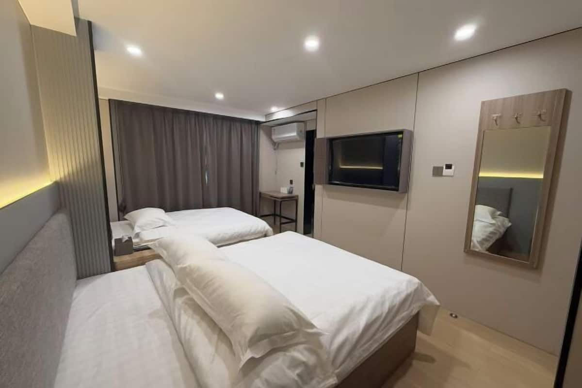 A modern hotel room with two beds, a flat-screen TV, a mirror, and a desk.