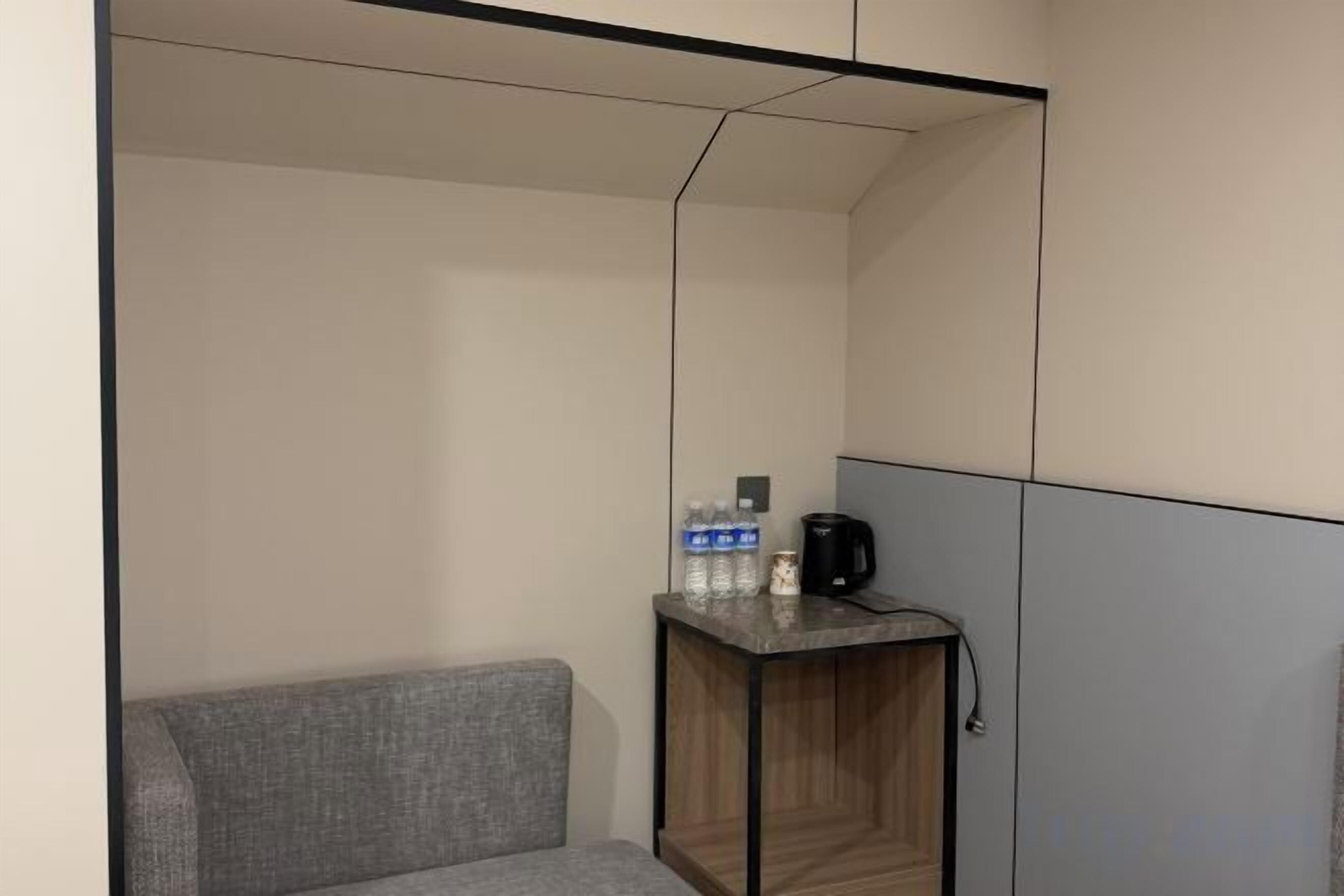 A modern hotel room with a grey sofa, a wooden side table with a coffee maker, and a flat-screen TV.