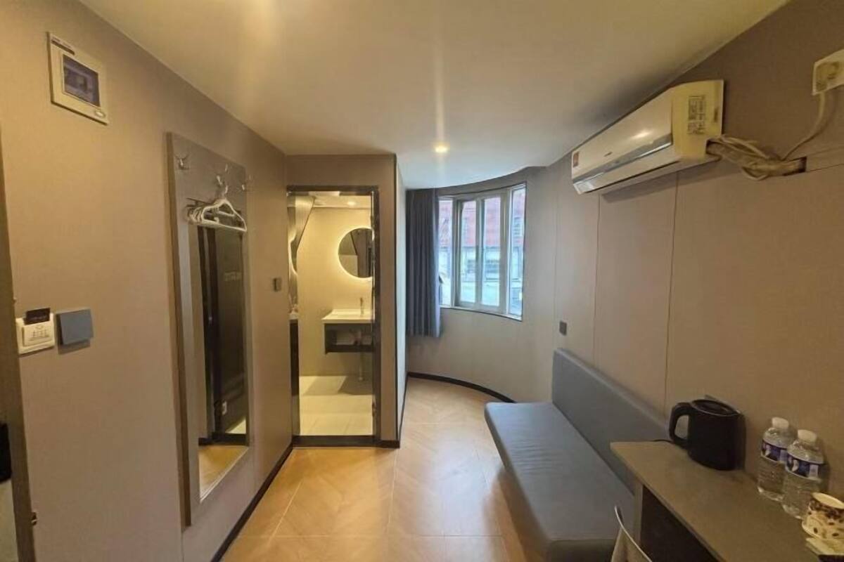A modern hotel room with a curved layout, a built-in bench, a small table with a coffee maker, and a window providing natural light.