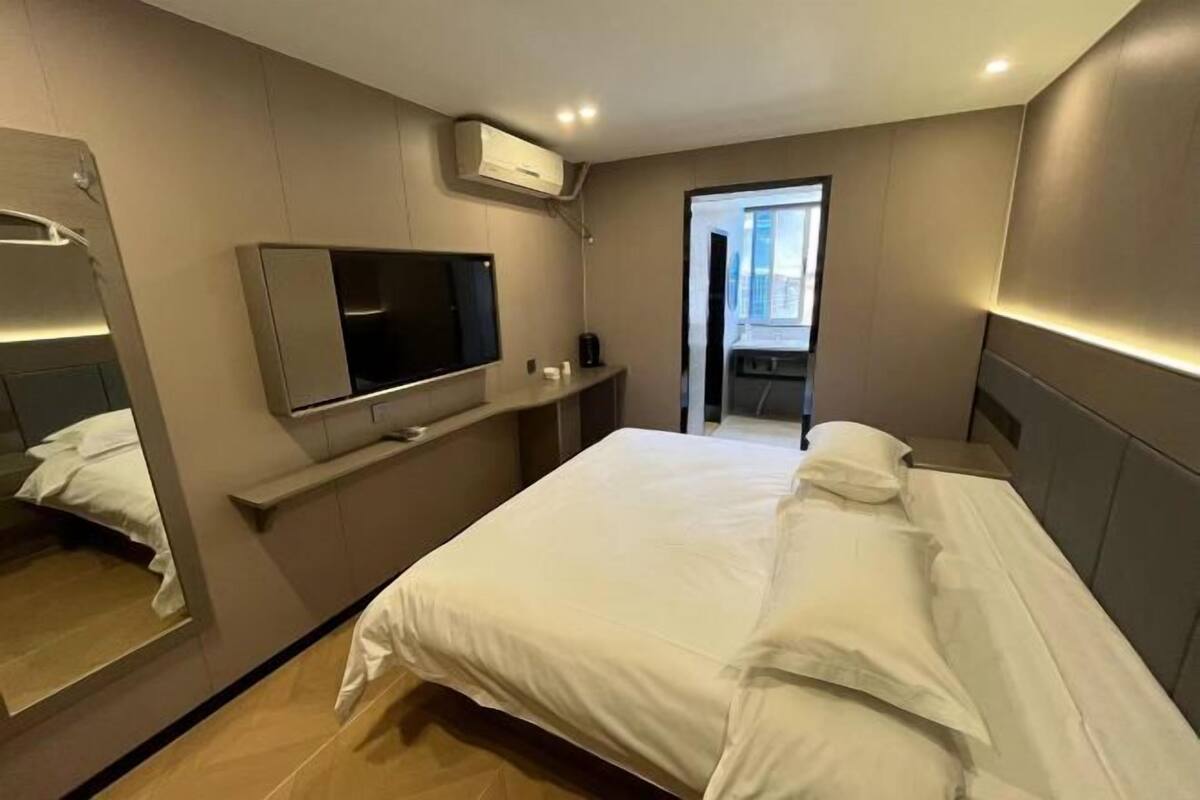 A modern hotel room with a large bed, a mounted TV, and a small seating area.