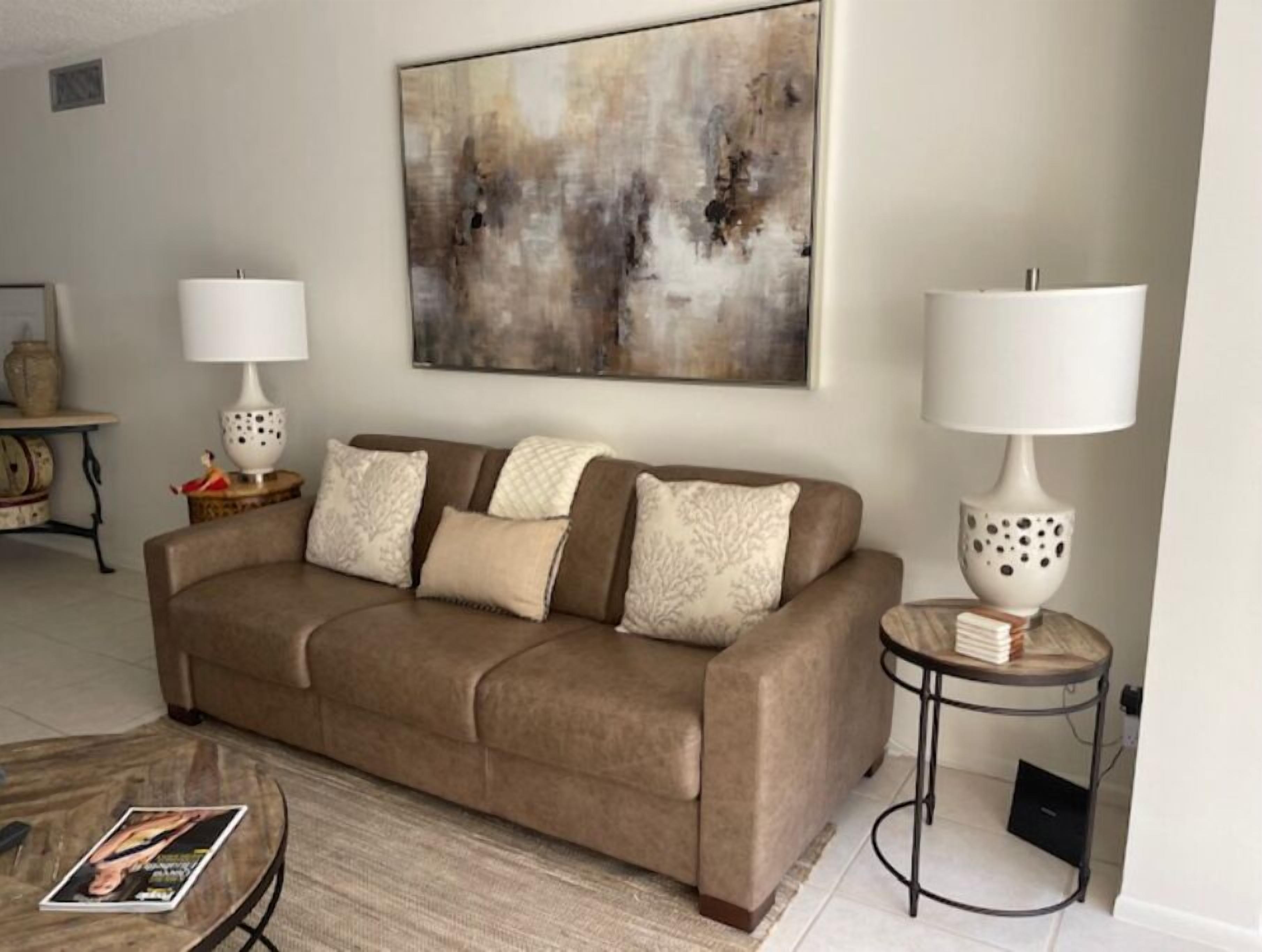 A living room with a brown sofa, two side tables with lamps, a coffee table, and a large abstract painting on the wall.