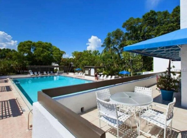 A rooftop pool area with a clear blue sky, a pool, lounge chairs, and a table with chairs.