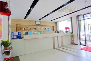 A reception desk with a 'Welcome' sign, a potted plant, and a red mat.