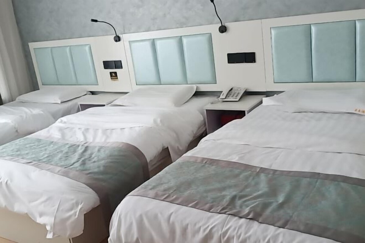 A hotel room with three beds, each with a headboard and bedside tables.