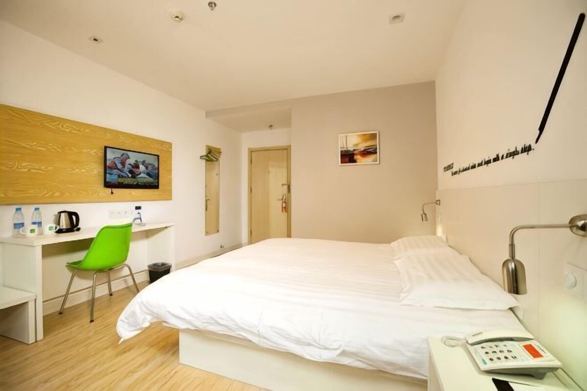 A hotel room with a bed, a desk, a chair, a telephone, and a wall-mounted TV.